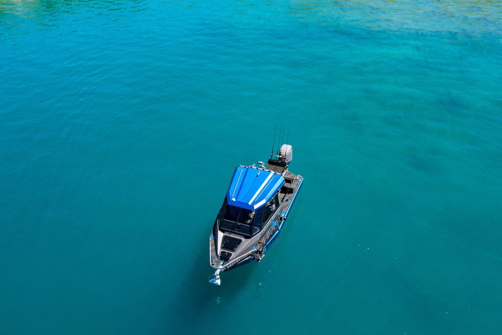 Close top-down drone view of fishing boat on Lake Hāwea surrounded by clear blue water