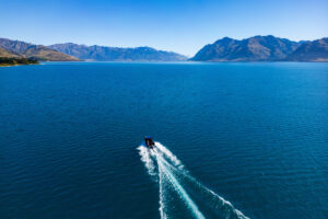 Drone photo from above showing fishing boat on Lake Hāwea with surrounding mountains