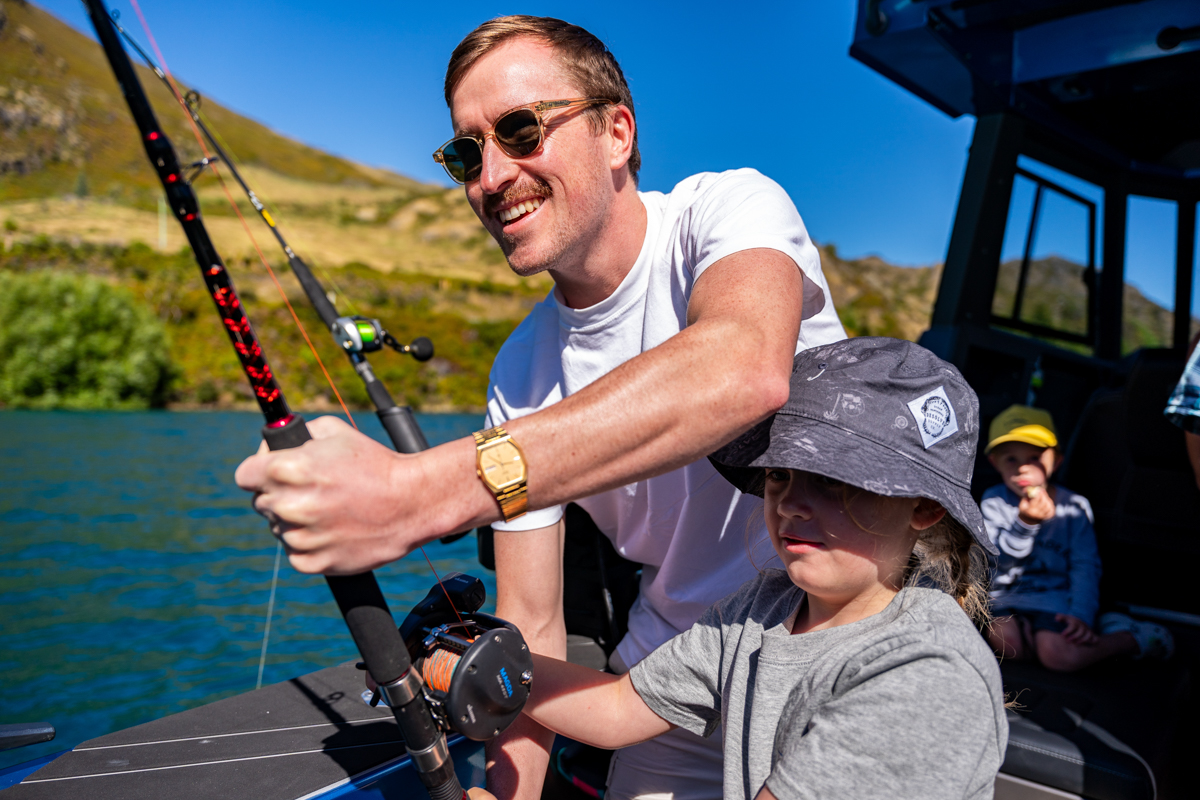 Father and child holding a fishing rod together on a boat during a charter in New Zealand