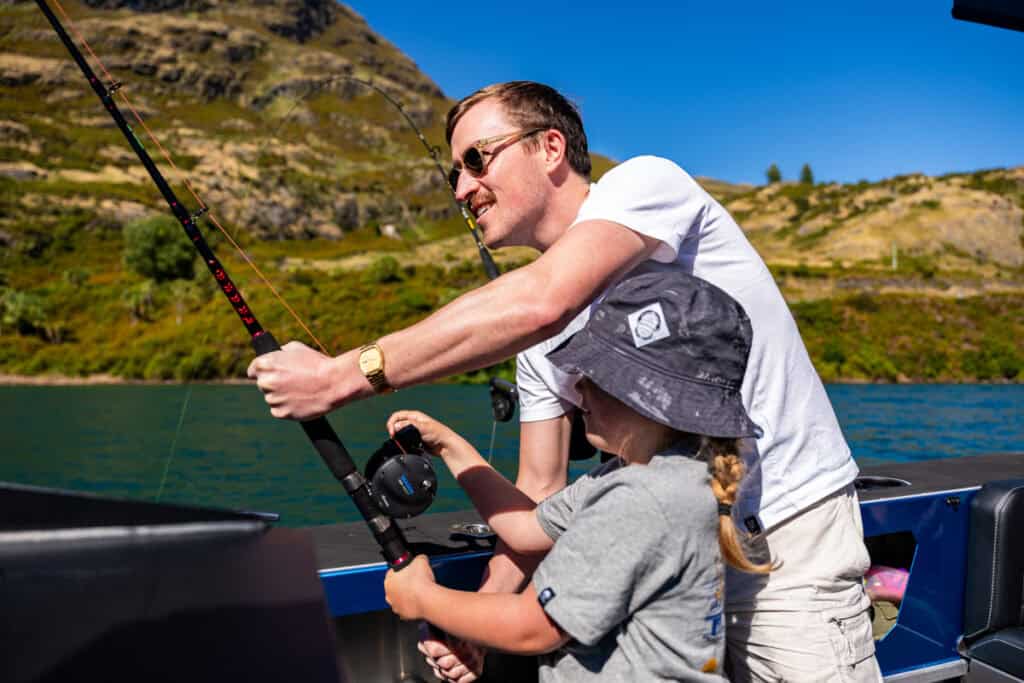 Father and child holding a fishing rod together on a boat during a New Zealand fishing charter