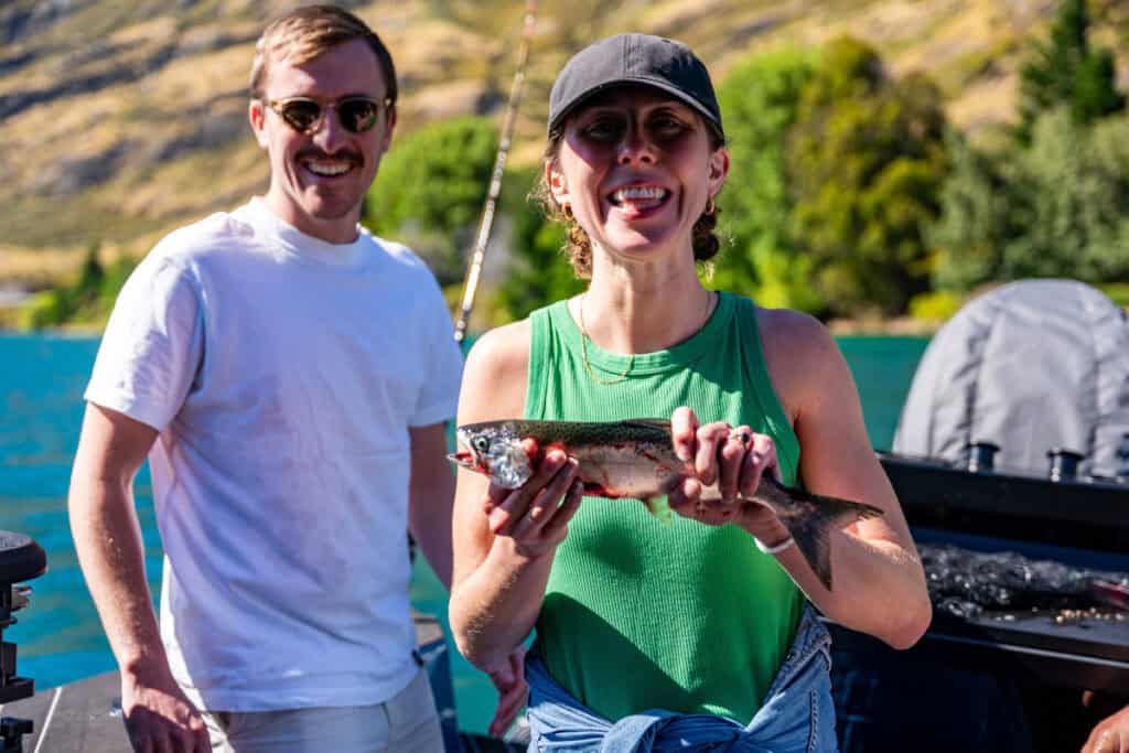 Woman showing off her freshly caught fish on a boat at Lake Hāwea, New Zealand