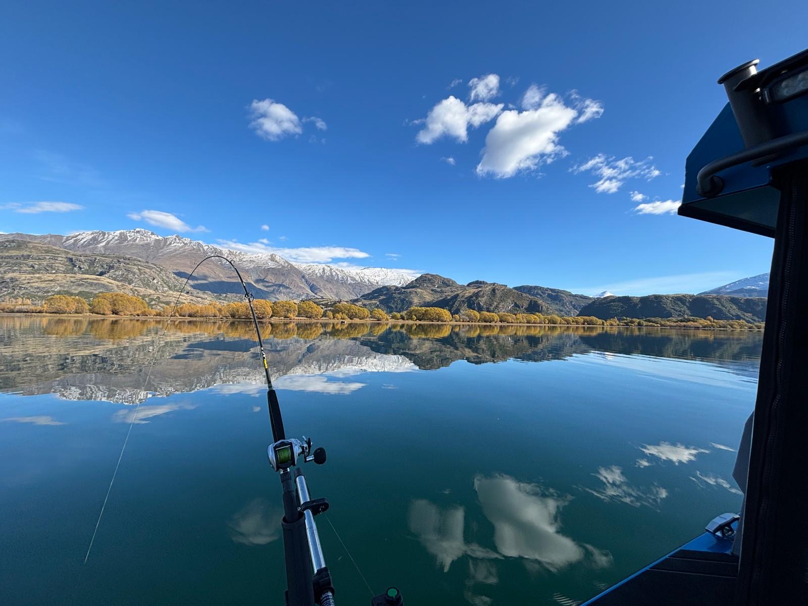 Flat lake surface with mountain backdrop and fishing rod in the foreground during a New Zealand charter