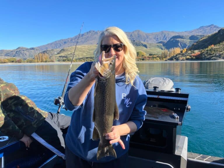 Woman proudly holding a large brown trout on a fishing charter at Lake Wānaka