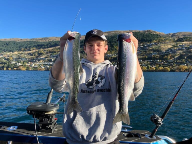Young man proudly holding up two trout caught at the same time during a New Zealand fishing charter