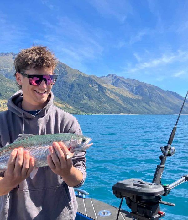 fishing-success-trout-hold-lake-nz Happy angler holding a trout with alpine scenery in the background
