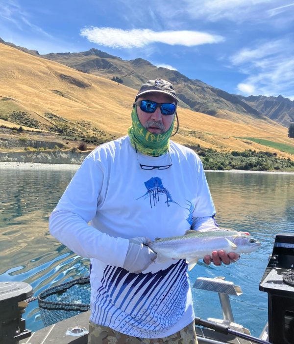 hunter-catch-fish-lake-hawea-nz-charter Hunter holding his catch on a charter boat with Lake Hāwea in the background