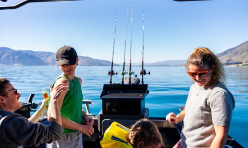 people-on-boat-ready-fishing-rods-calm-water-nz People on the back of a fishing boat with rods in holders and calm lake water