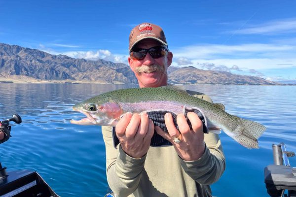 private-charter-hunter-rainbow-trout-sunny-day Hunter smiling with a rainbow trout catch on a beautiful day at Lake Hāwea