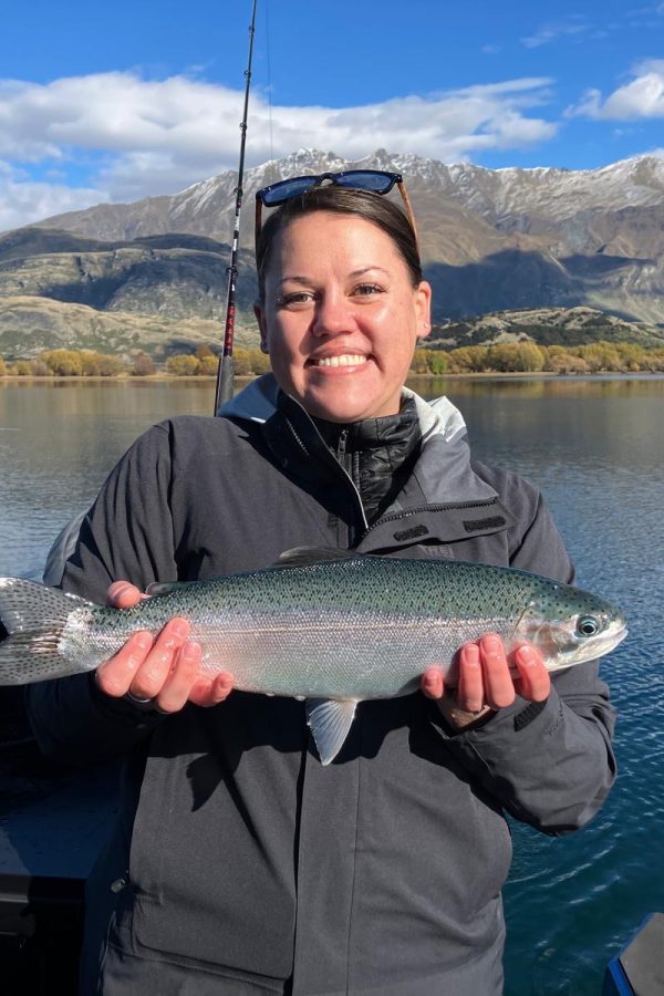 woman-holding-trout-lake-wanaka-fishing-charter Woman proudly holding a trout with Lake Wānaka and mountains in the background