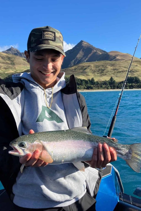 young-angler-holding-large-rainbow-trout-lake-hawea Young man holding a large rainbow trout in bright sunlight on Lake Hāwea